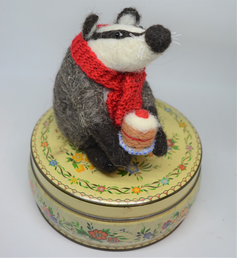 Badger wearing red scarf holds cake.